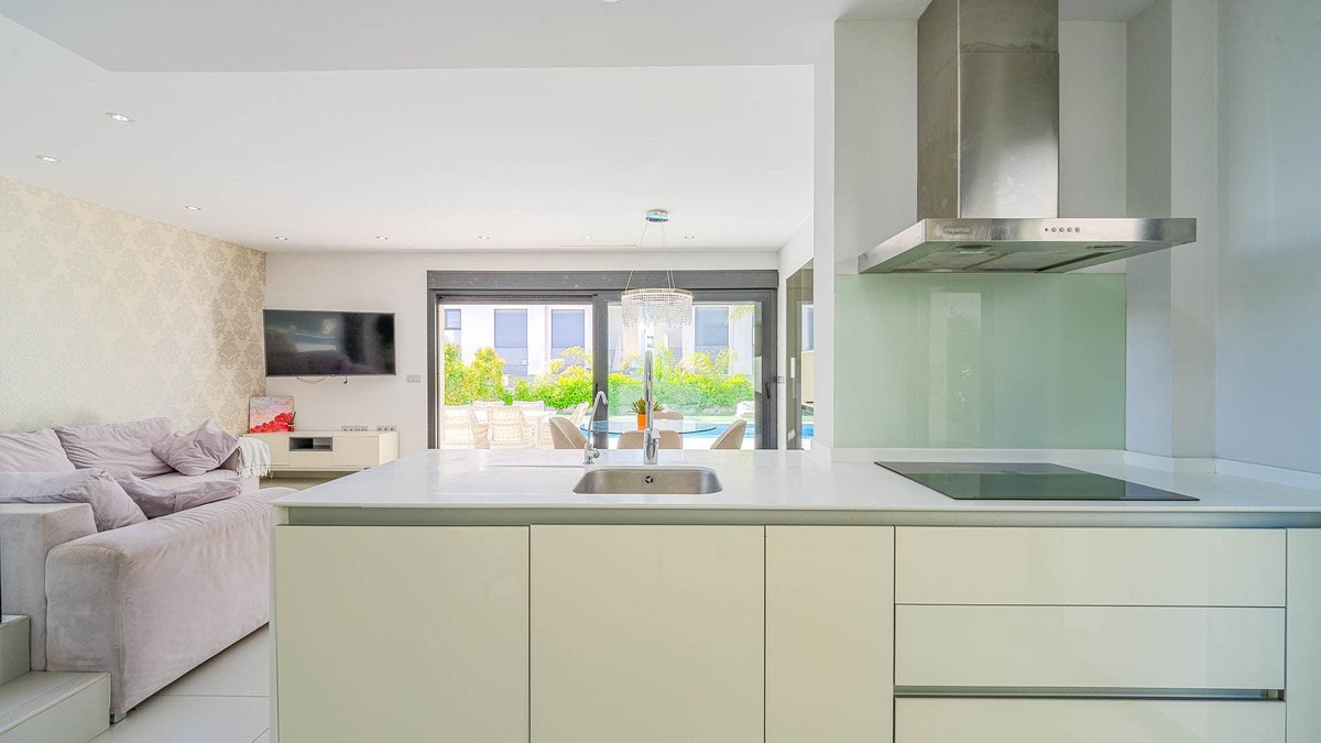 Modern open-plan living space with a sleek kitchen, comfortable sofa, and a view of the pool area through large sliding doors.
