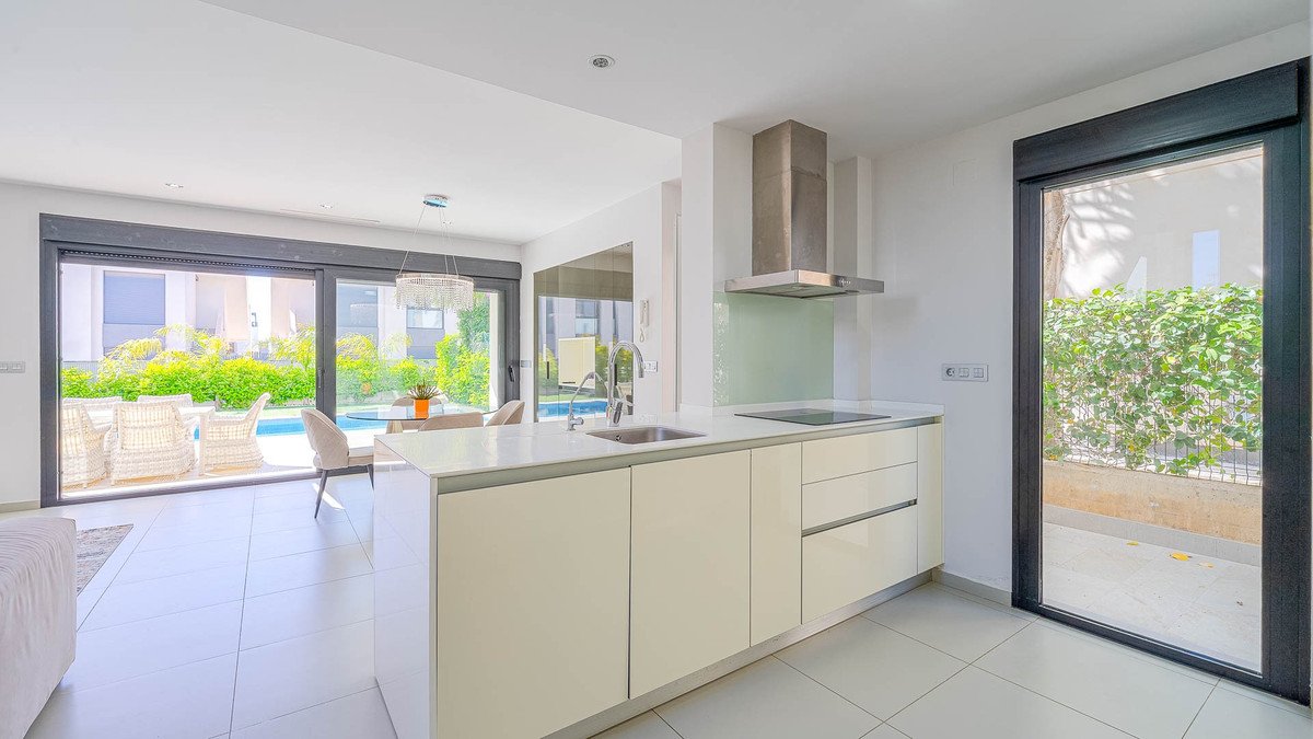 A modern kitchen with a sink and stovetop, opening to a dining area with a pool and garden view.
