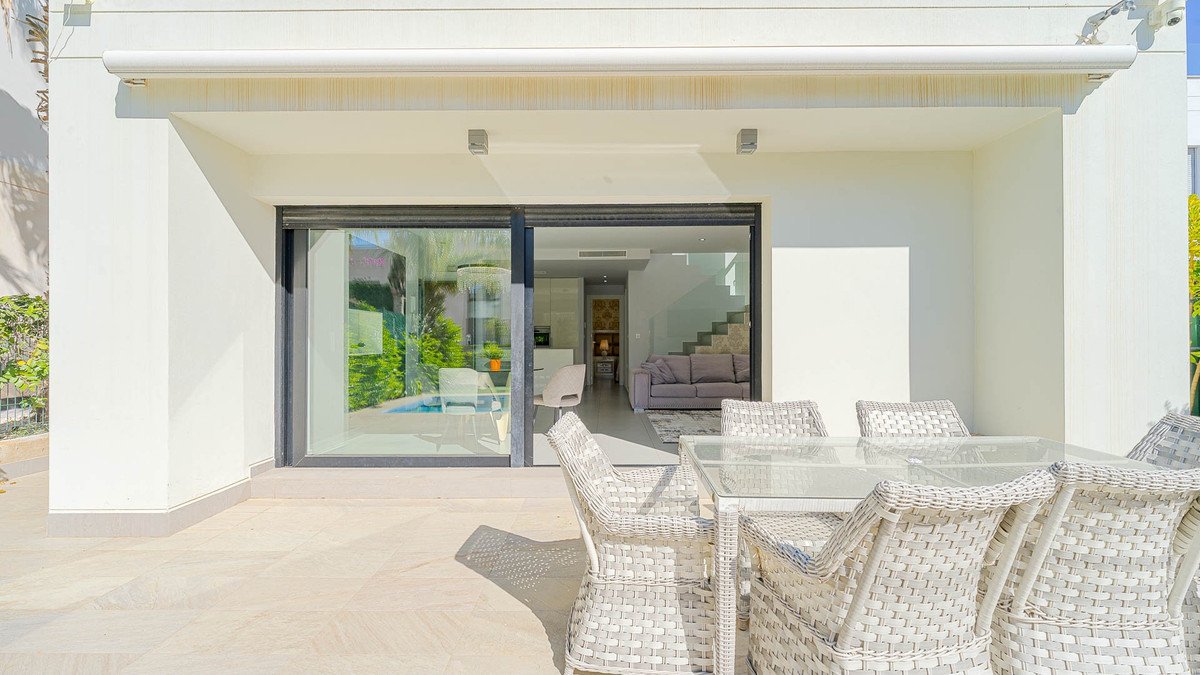 Outdoor dining set on terrace with view of a pool and modern interior through sliding glass doors.
