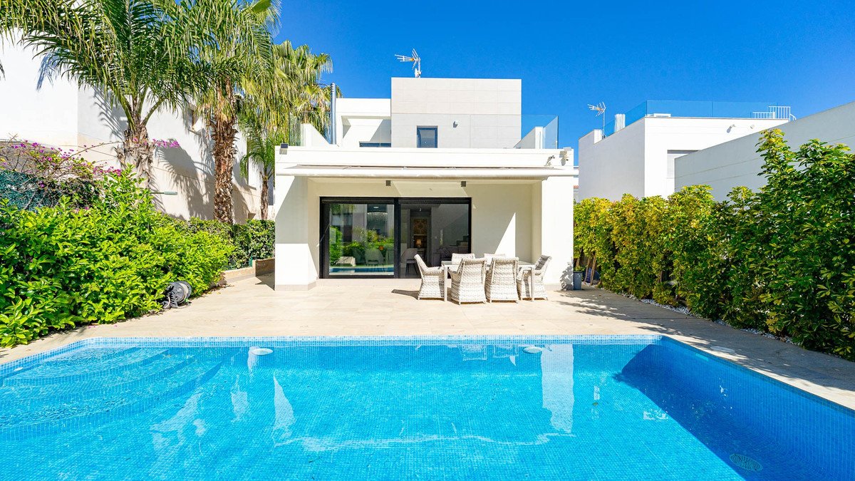 A modern villa with a private pool and an outdoor dining area on a tiled patio, surrounded by lush greenery and palm trees.
