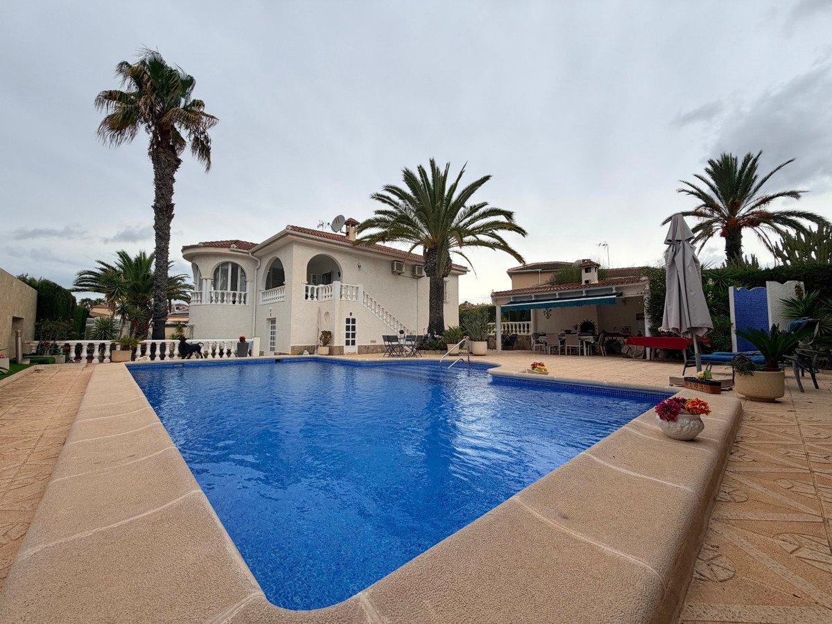 Spacious villa with a large blue swimming pool, surrounded by palm trees and outdoor seating areas.