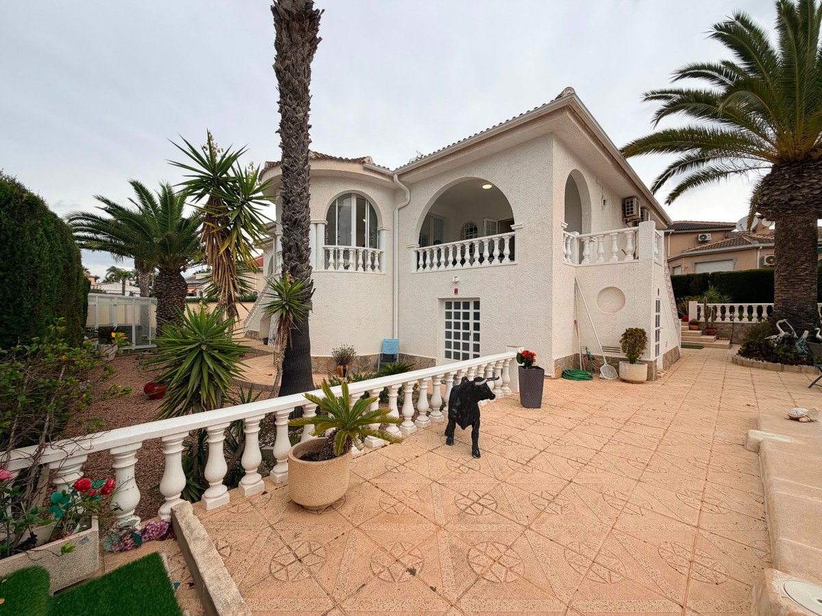 Exterior of a white villa with a large tiled terrace, surrounding palm trees, and a black bull statue on the patio.