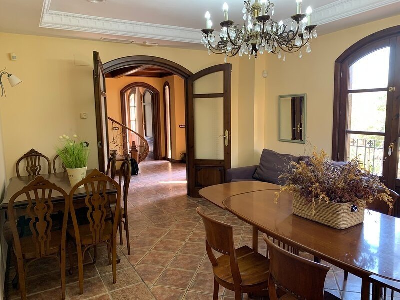 Dining and living area with a chandelier, ornate chairs, and a view of a spiral staircase through an archway.