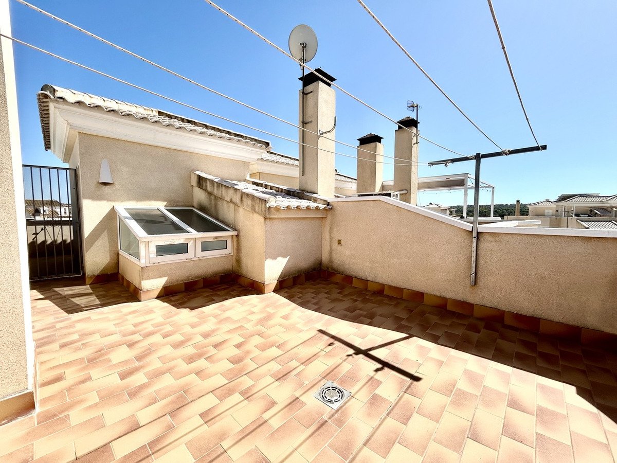 A tiled rooftop terrace with a clothesline, skylights, and a metal gate overlooking a residential area under a clear blue sky.