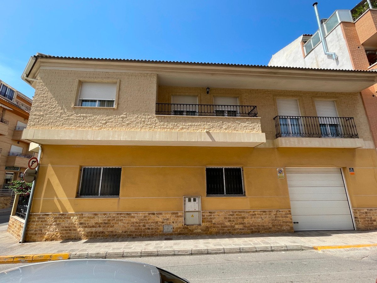 A yellow two-story house with balconies, security bars on windows, and a large garage door under a clear blue sky.