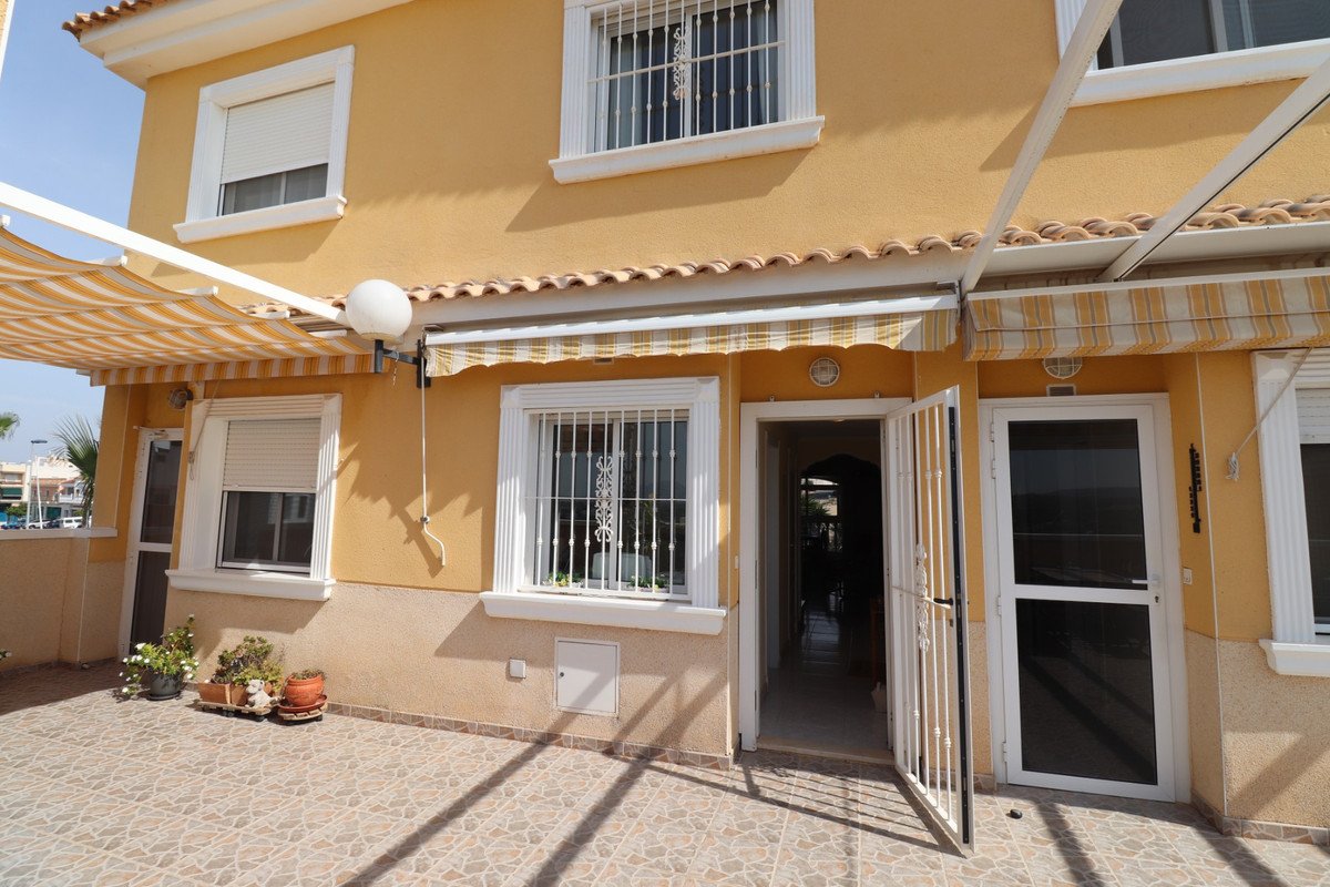 Exterior view of a house featuring a tiled patio with awnings, an open doorway, and barred windows.
