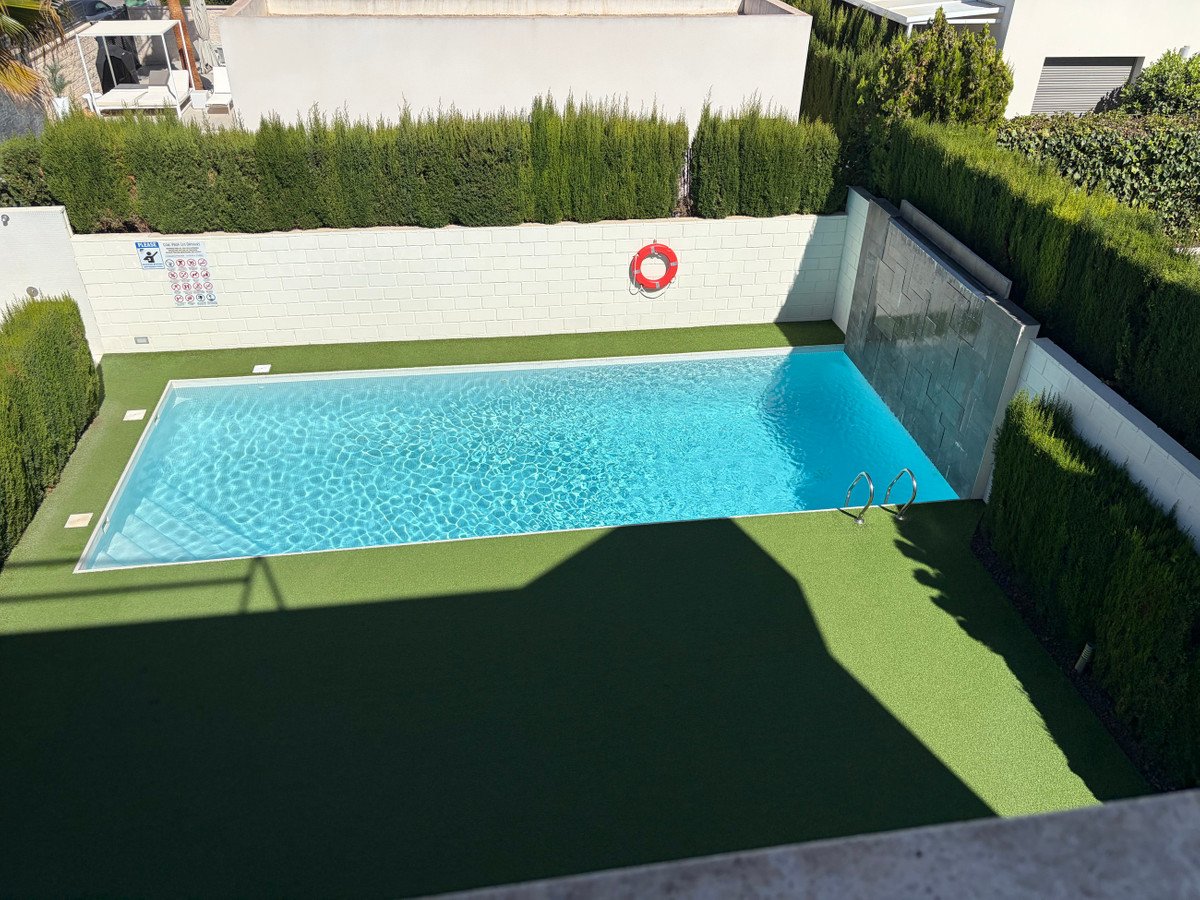 A clean swimming pool with clear blue water, surrounded by artificial grass and a decorative waterfall feature on the wall.