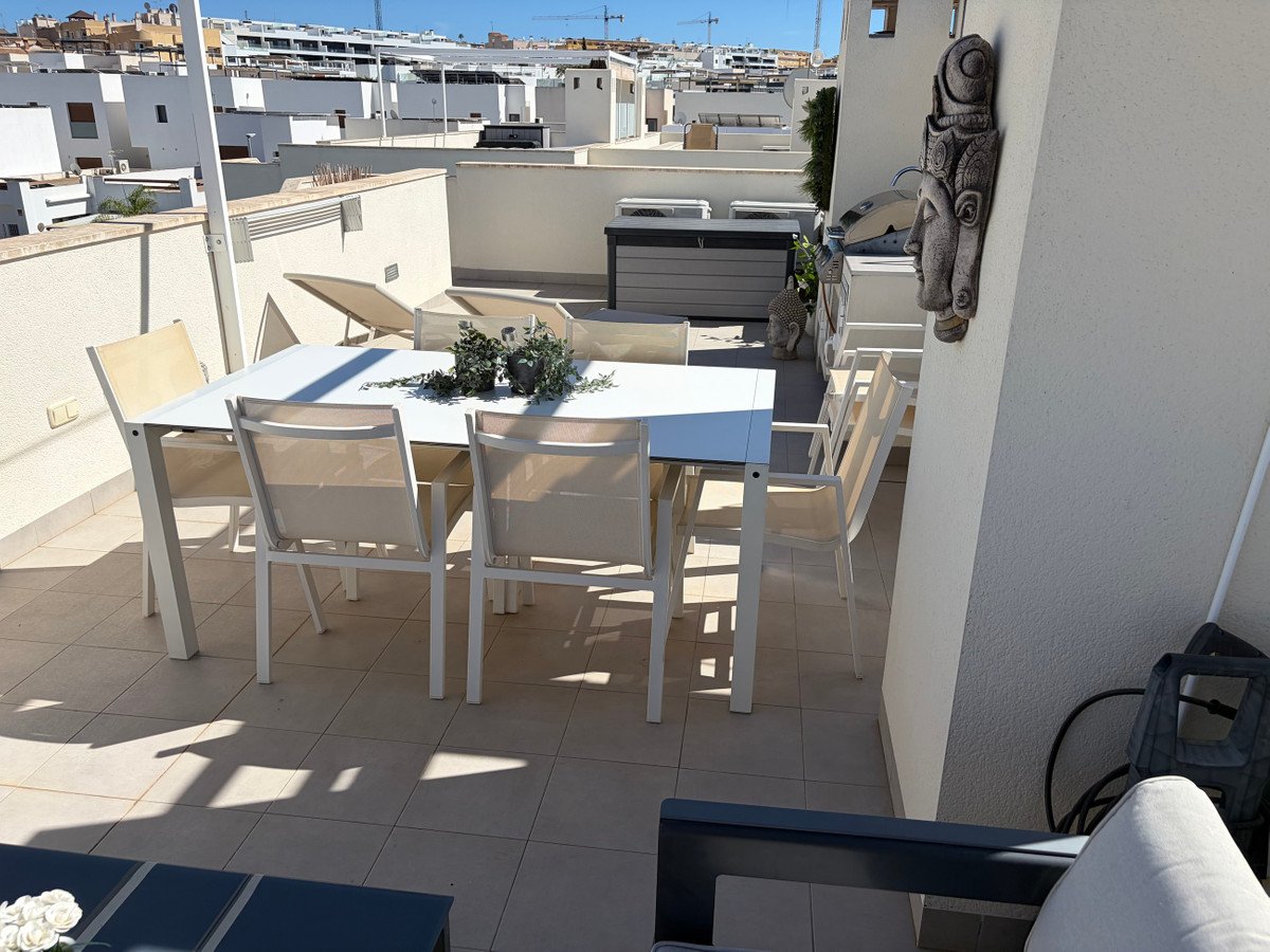 Terrace with white dining table and chairs, decorative Buddha head, and lounge chair. Sunny day.