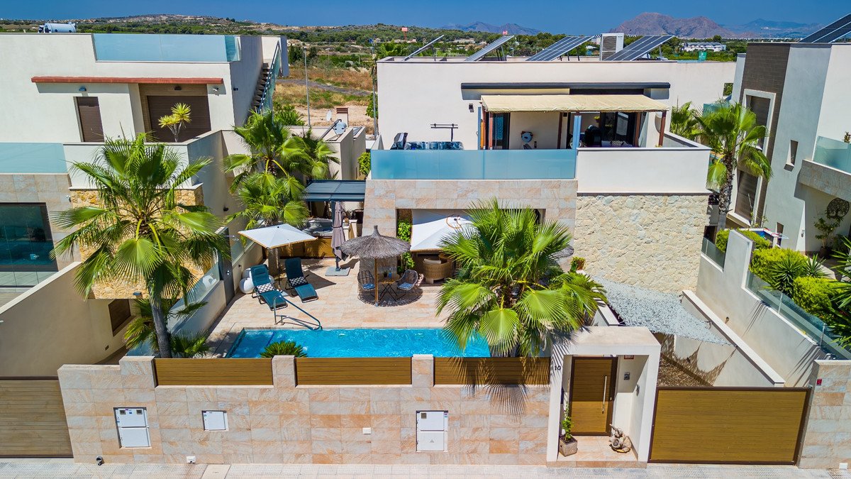 Modern villa with a private swimming pool, sun loungers, palm trees, and a covered seating area.