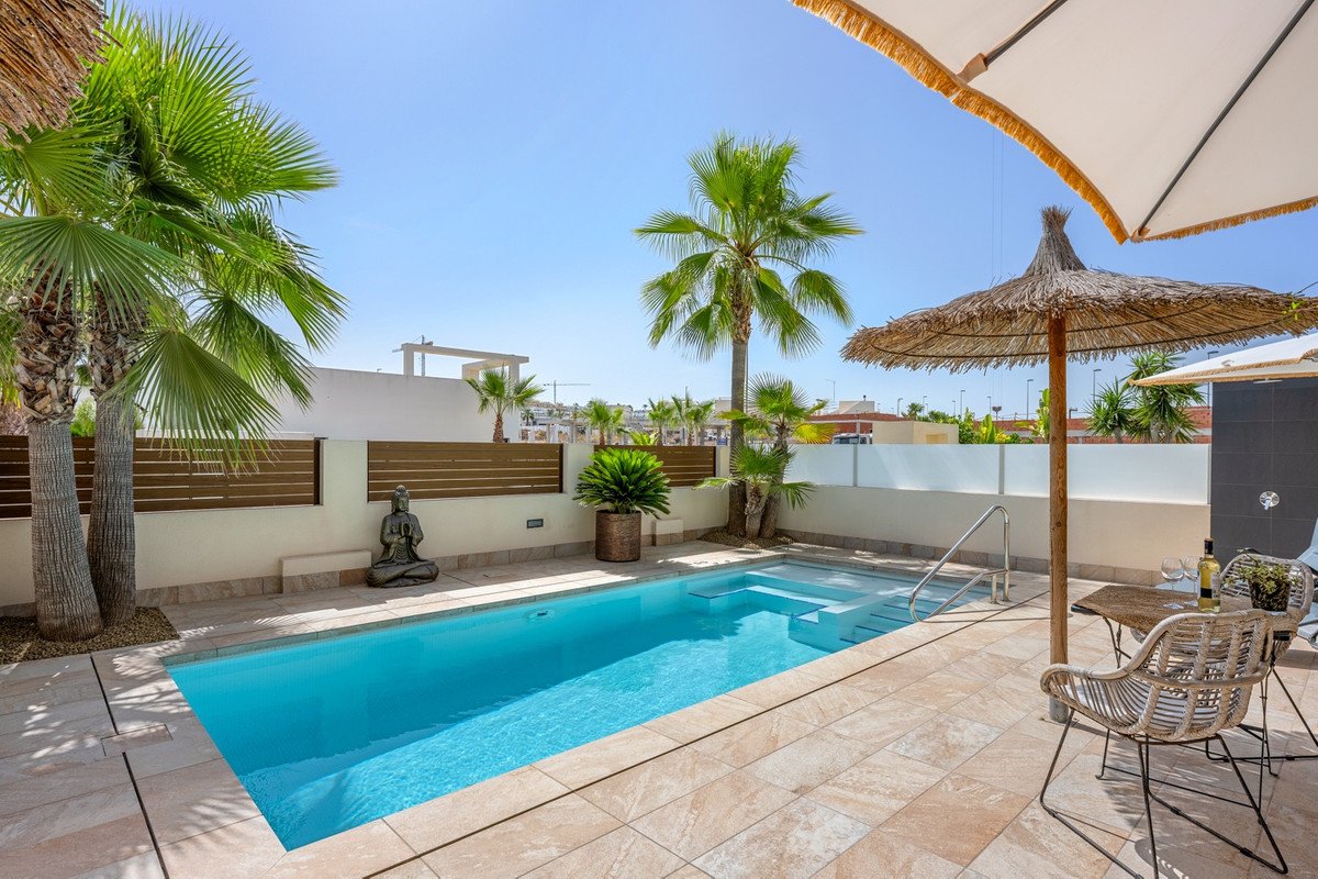 A private swimming pool with steps, surrounded by a tiled terrace, palm trees, and outdoor seating with umbrellas.