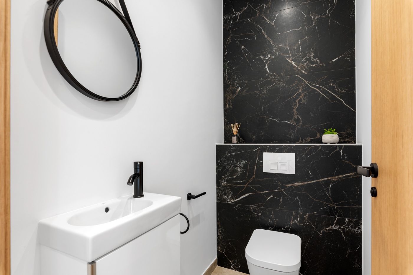 Moderne badkamer met zwarte marmeren tegels en witte wastafel.