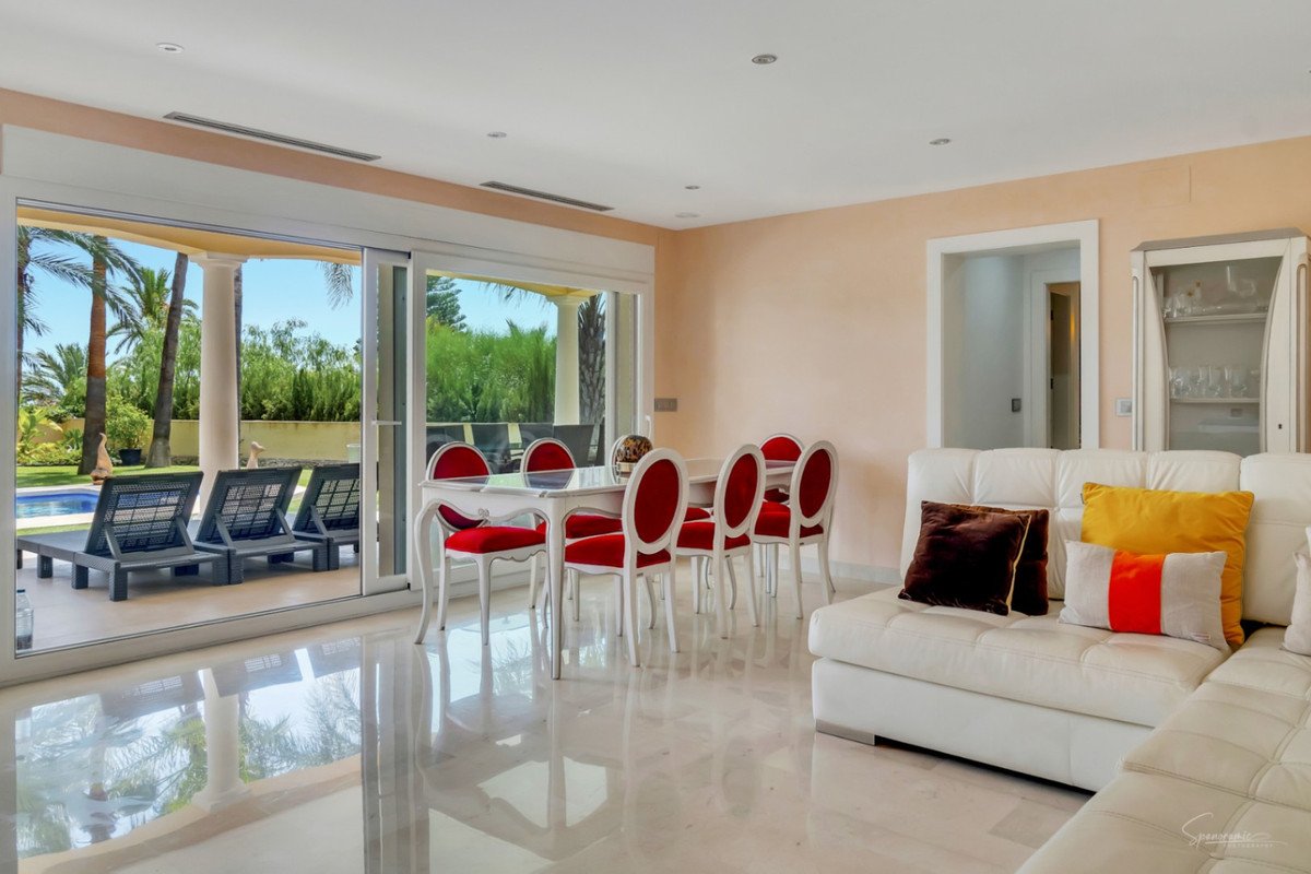 Bright living room with white sofa, red chairs, and view of swimming pool and palm trees
