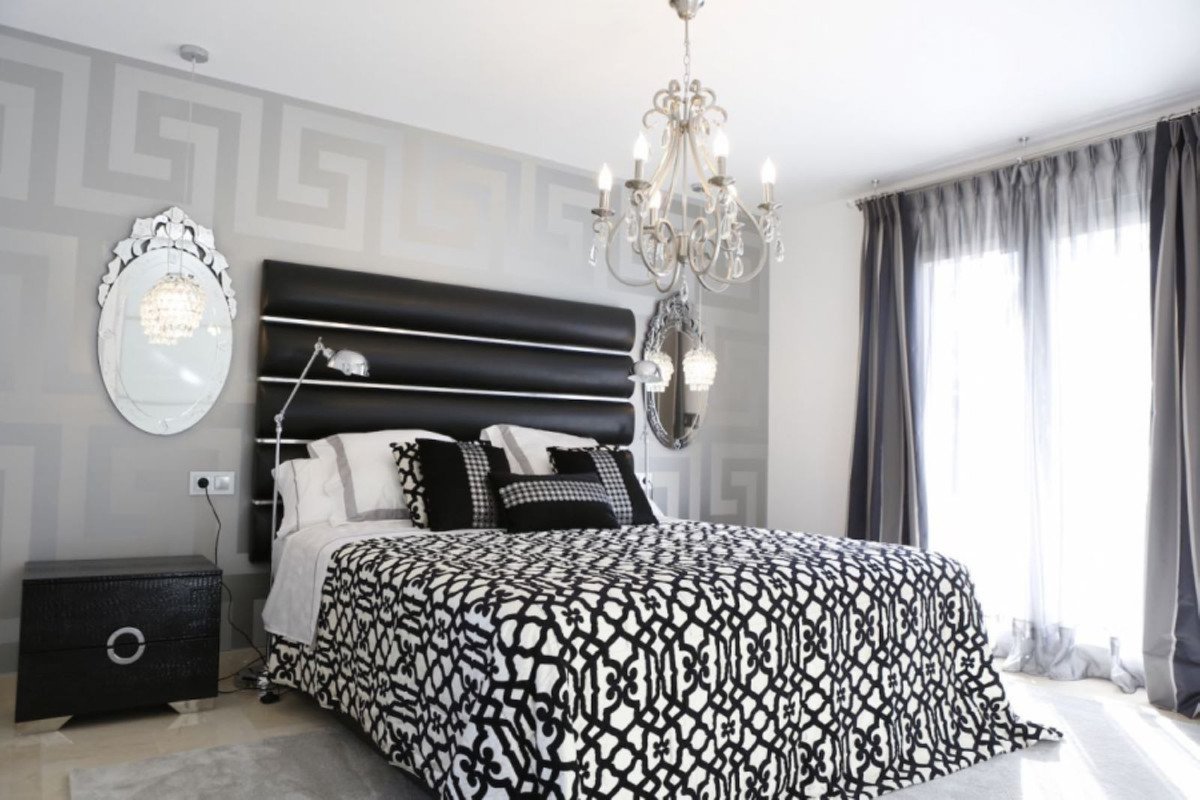 Modern bedroom with black and white geometric bedding, chandelier, and patterned walls.