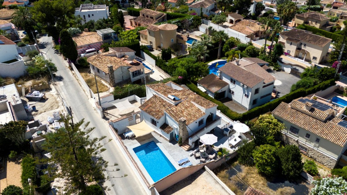 Aerial view of a villa with a pool, terracotta roof, and garden in a residential area.