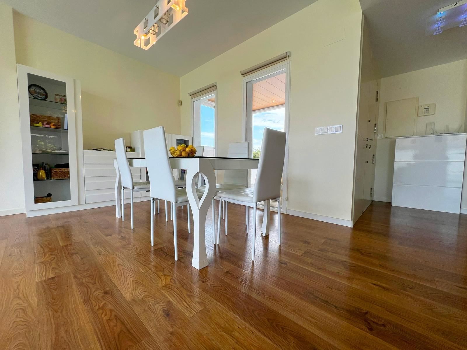 Moderne eetkamer met witte stoelen en houten vloer.