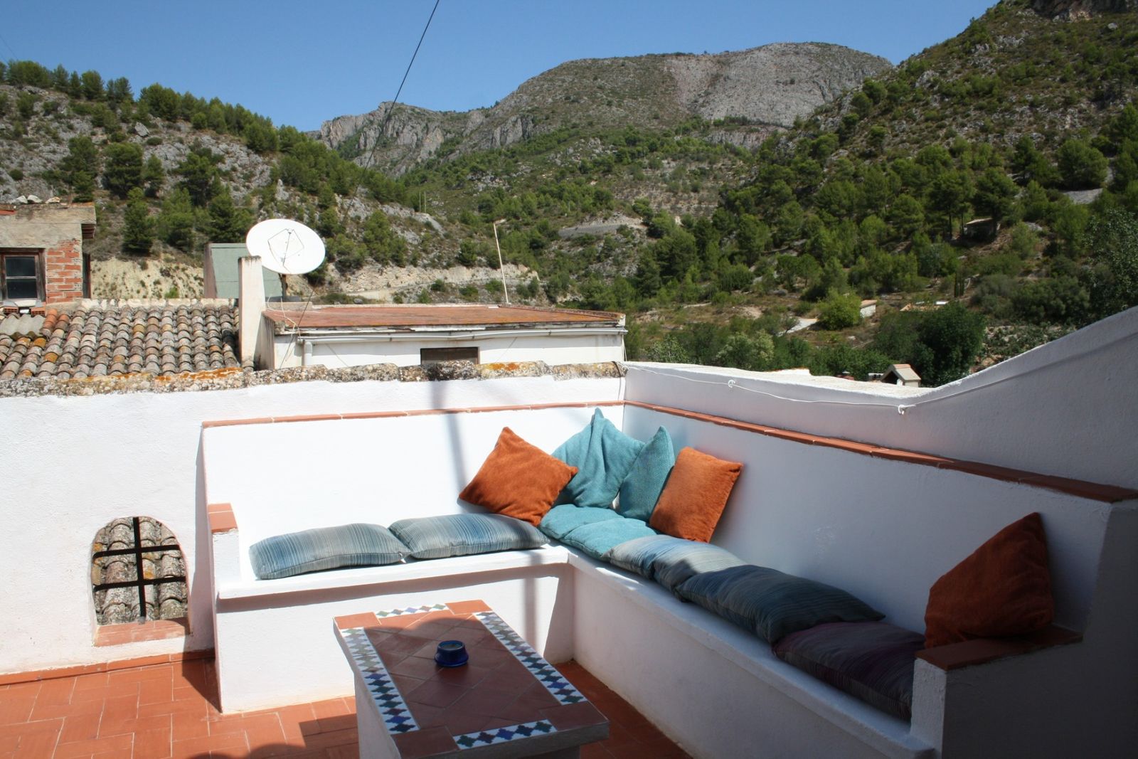 Terras met uitzicht op de bergen, zitbank en tafel met kussens.