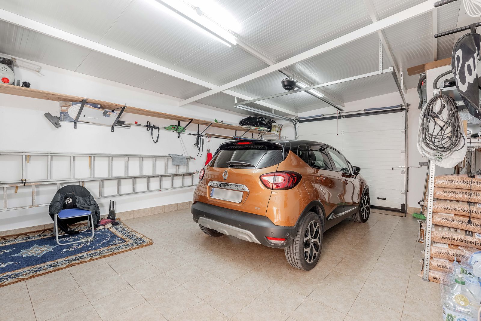 Georganiseerde garage met auto, ladder en opbergruimte.