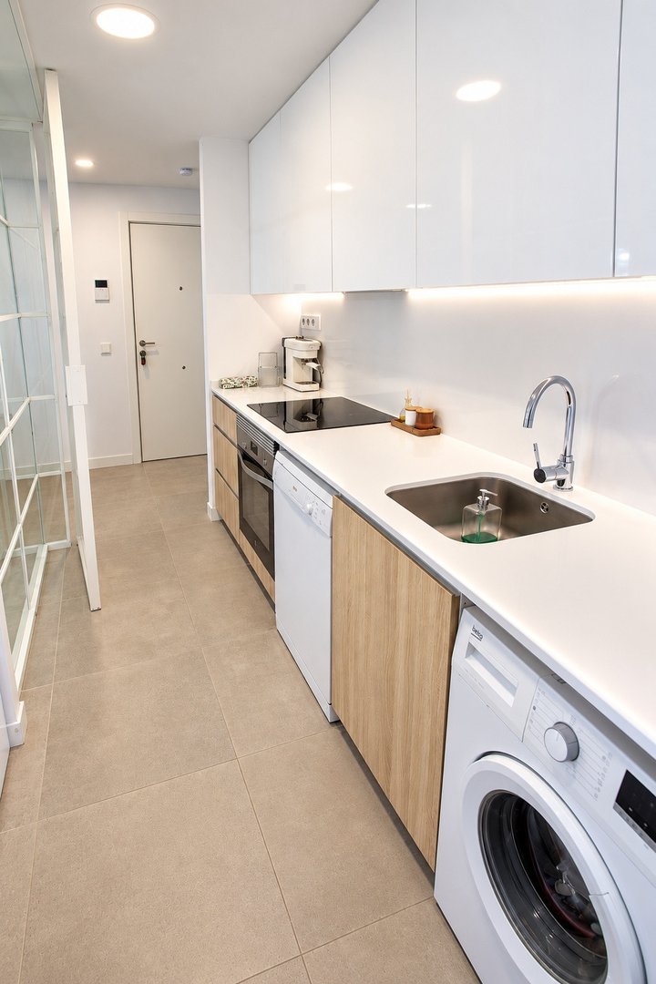 Modern galley kitchen with white cabinets, induction hob, sink, oven, dishwasher, and washing machine.