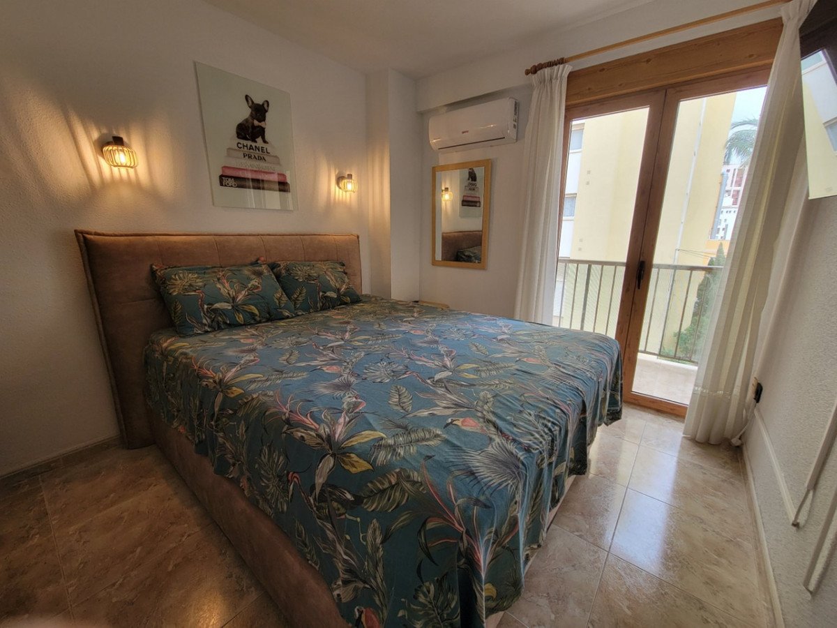 A bedroom with a large bed, tropical print bedding, wall art, and a door leading to a balcony with a railing.
