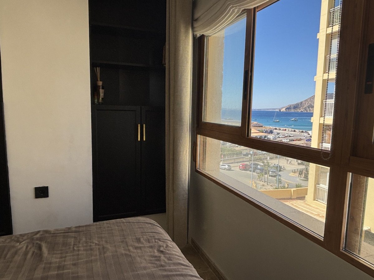 Bedroom with a built-in wardrobe and a large window offering a stunning sea view with boats and a coastal town.