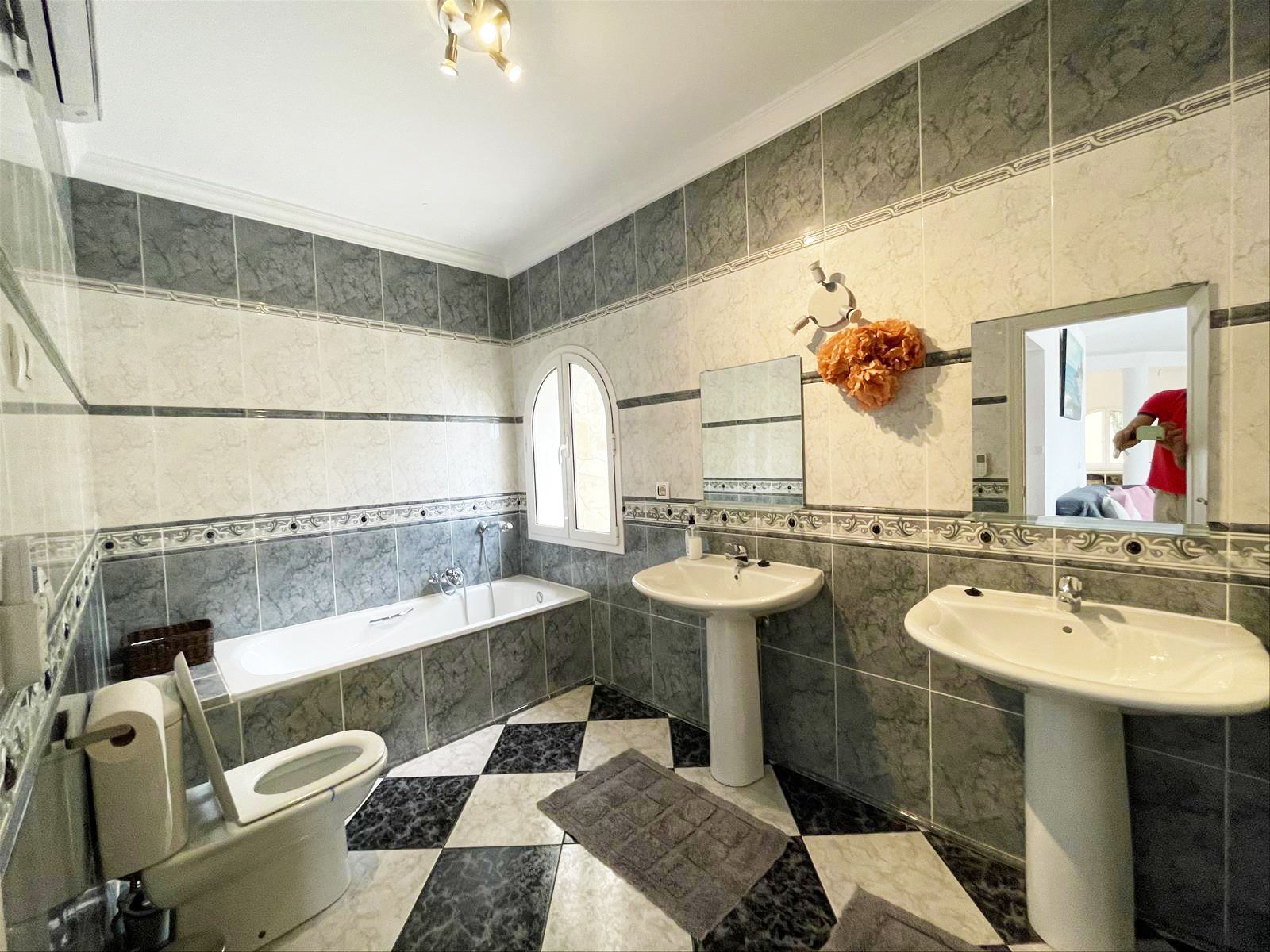 Badkamer met zwart-wit geblokte vloer, bad, twee wastafels en grijze tegels