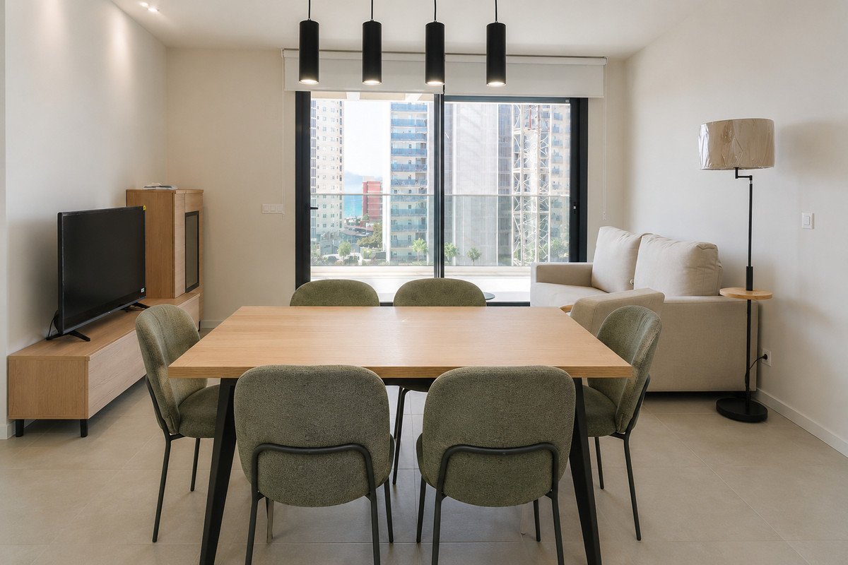 Modern dining room with wooden table and green chairs, adjacent to a living area with a sofa, offering a city view through large windows.