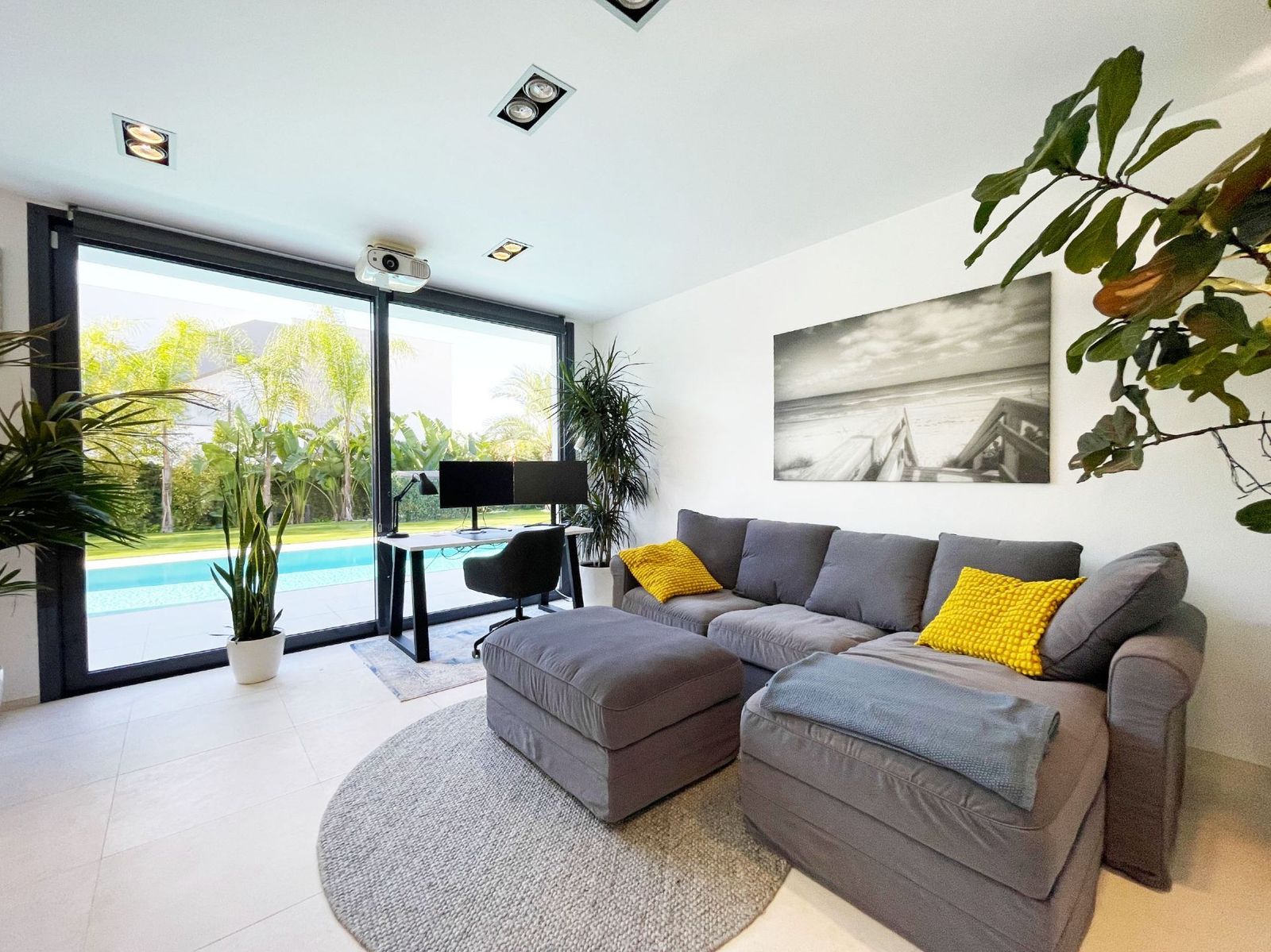 Moderne woonkamer met uitzicht op het zwembad en een grijze hoekbank.