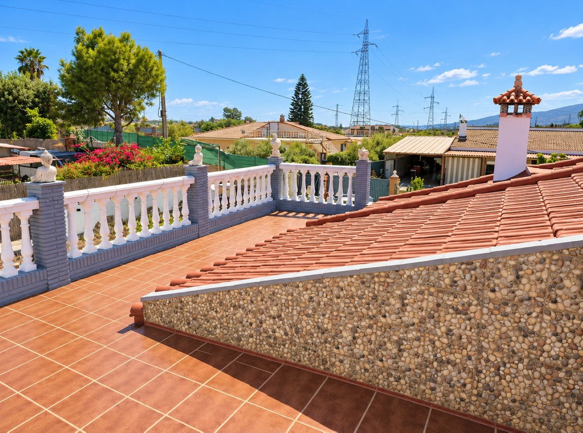 Tiled terrace with white balustrade and view of houses, trees, and distant power lines under a blue sky.