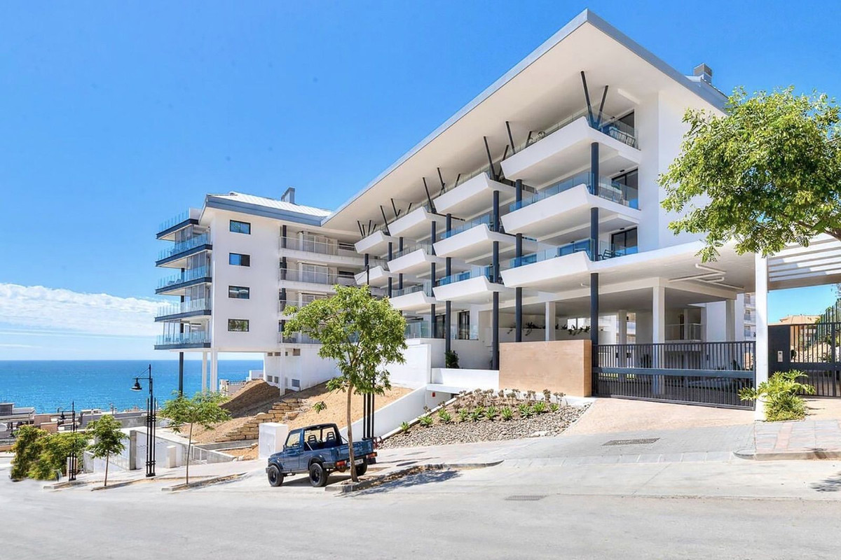 Modern appartementencomplex aan de kust met blauwe auto ervoor.