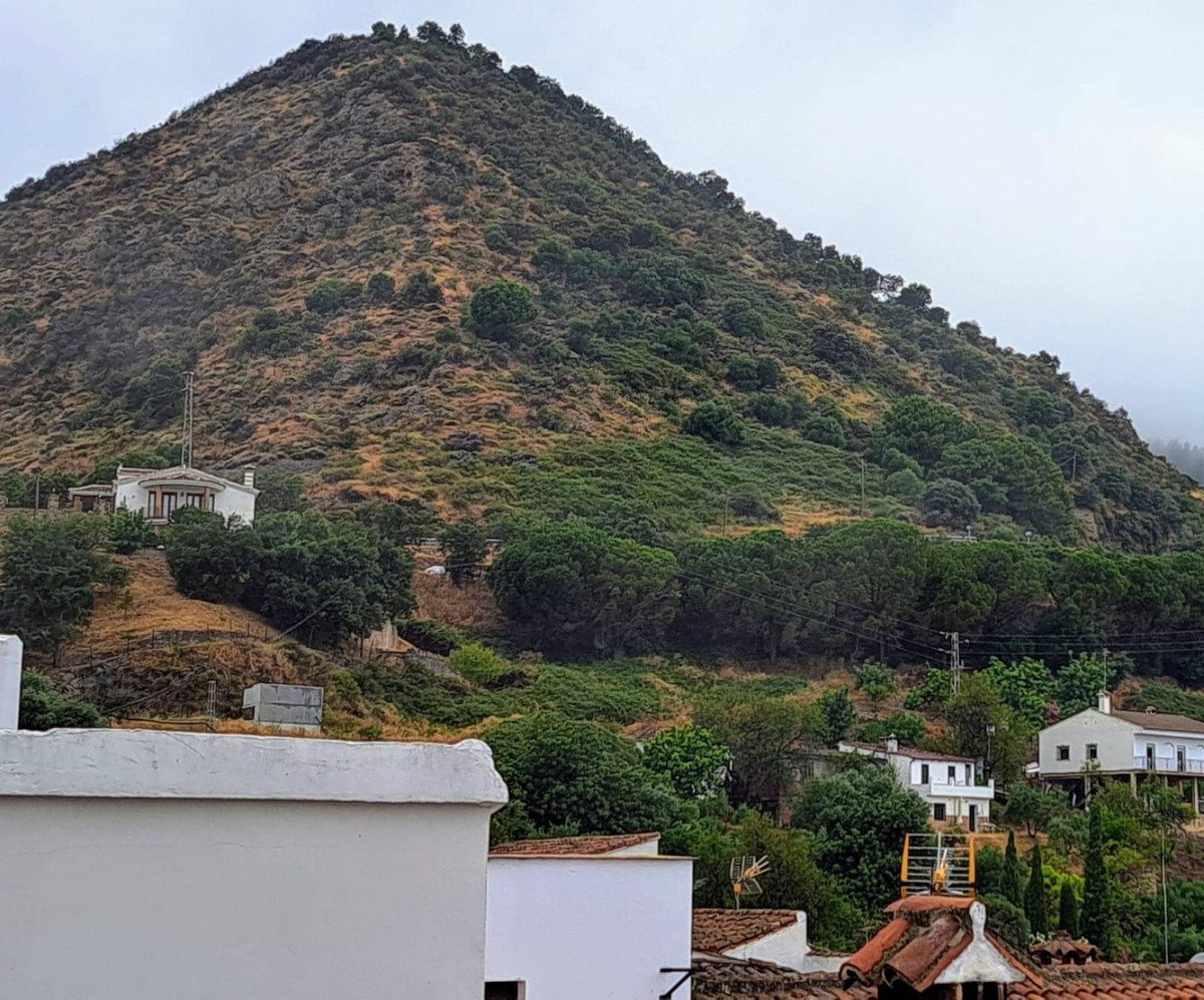 Houses nestled on a hillside with a lush mountain backdrop under a cloudy sky.