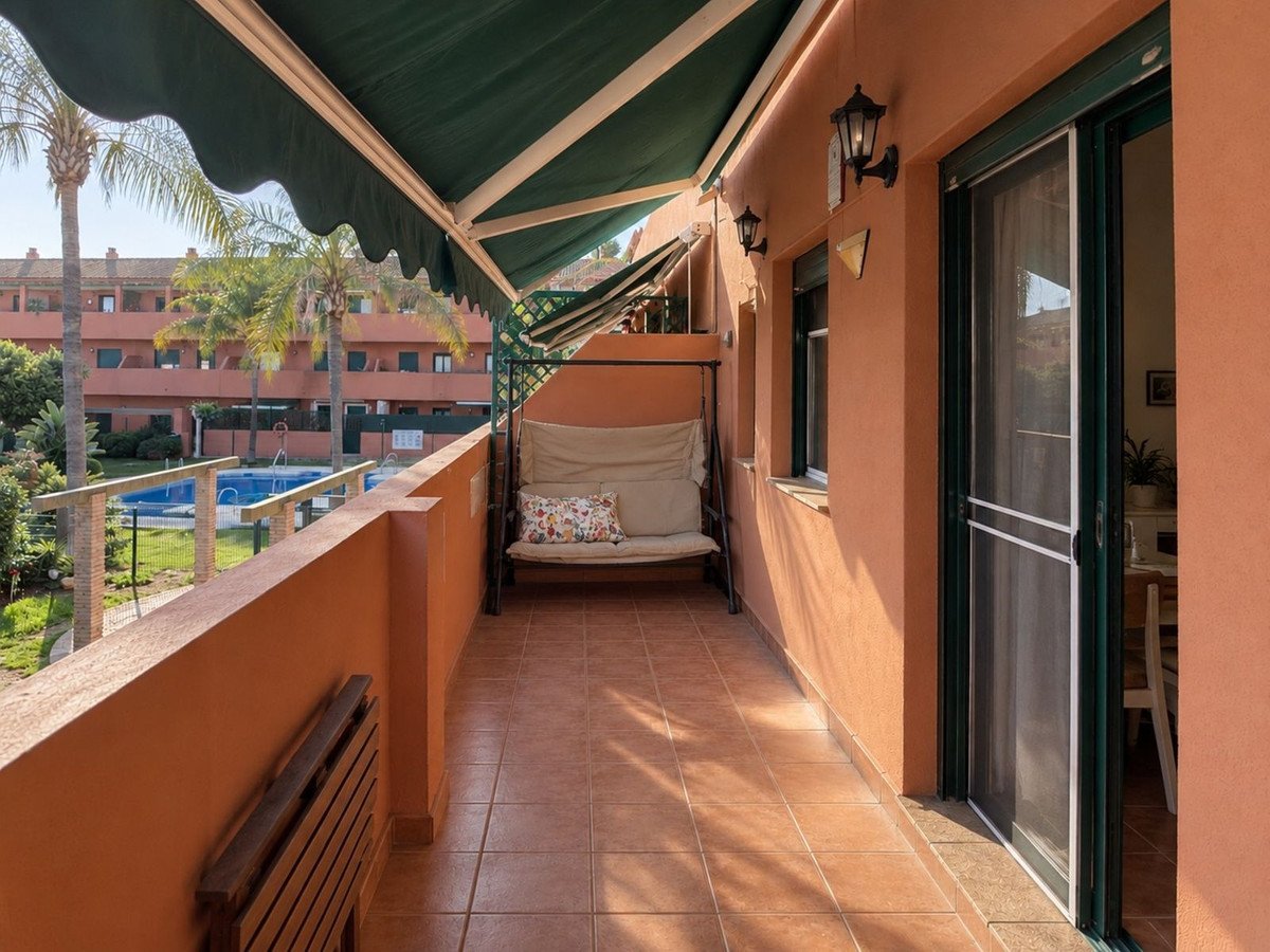 A sunny terrace overlooking a swimming pool, featuring a swing chair and a folding table.