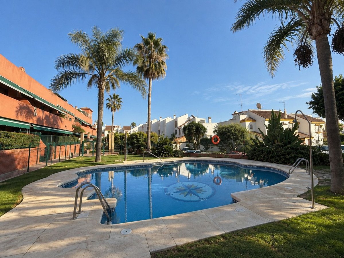 A curved swimming pool with a compass mosaic sits in a courtyard with palm trees and residential buildings in the background.