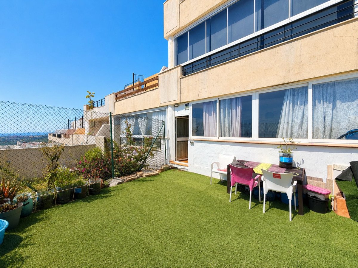 Terrace with artificial grass, table and chairs, overlooking a distant sea and town. Furnished outdoor space.