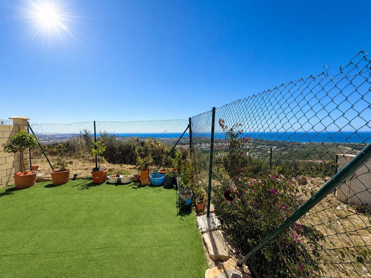 A fenced terrace with artificial grass, potted plants, and a scenic sea view on a sunny day.