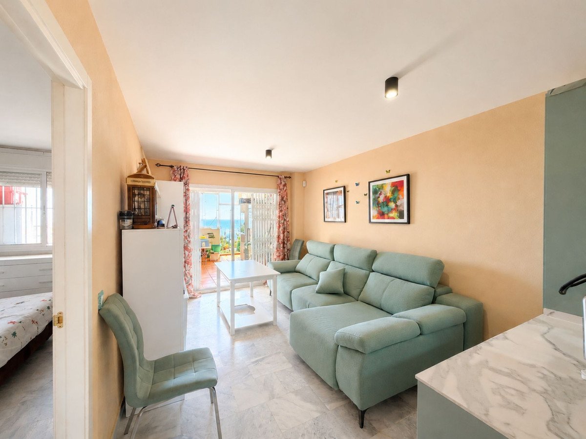 Light-filled living room with a pale green sectional sofa, coffee table, and access to a balcony with sea views.