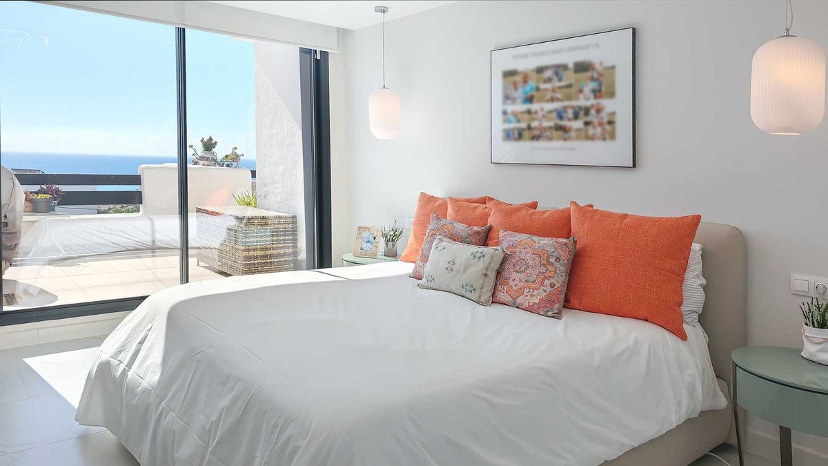 Modern bedroom with a large bed, orange accent pillows, and a balcony with a sea view through a glass sliding door.