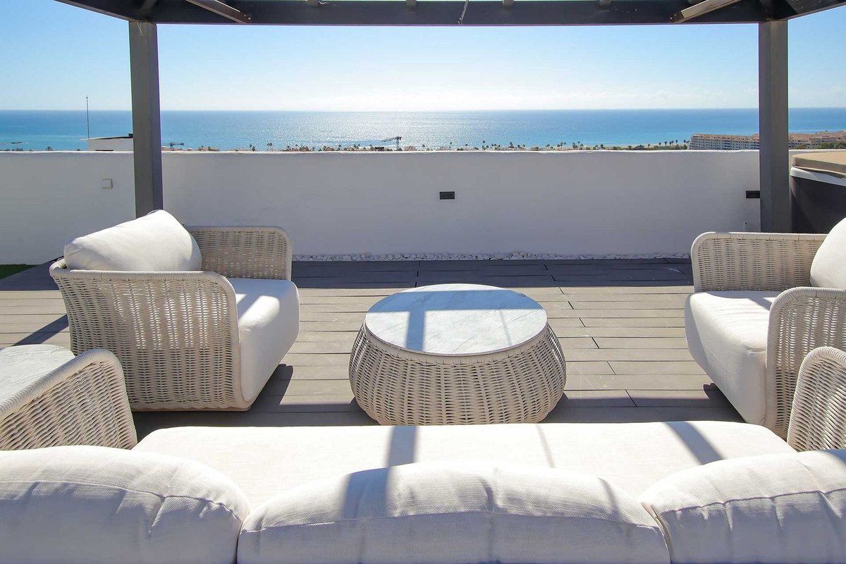 Rooftop terrace with white wicker seating and coffee table, offering a beautiful sea view.