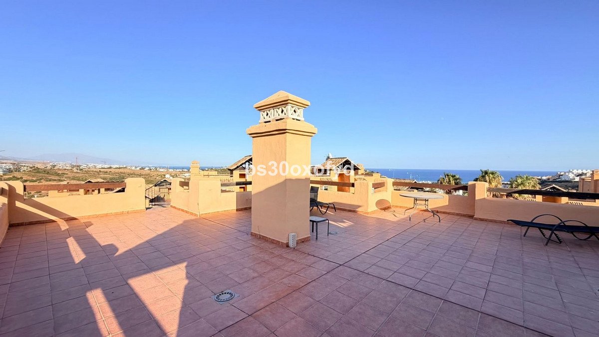 Spacious terrace with sea view, chimney, seating, and lounge chairs under a clear blue sky.