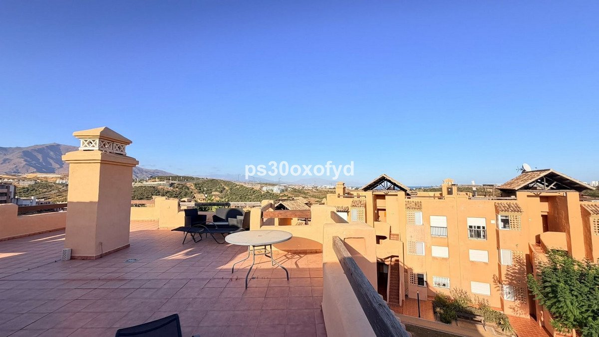 Terrace with chimney, outdoor table, chairs, and views of buildings and hills under a clear blue sky.