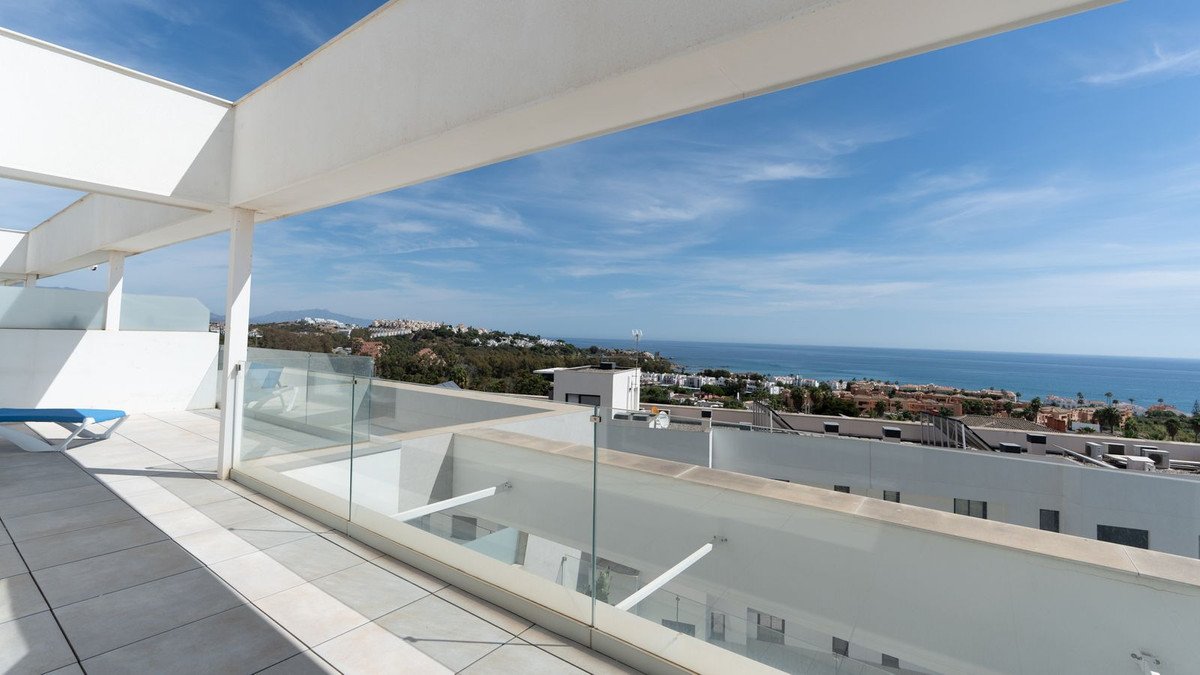 Spacious modern terrace with glass balustrade offering panoramic sea and coastal views under a clear blue sky.