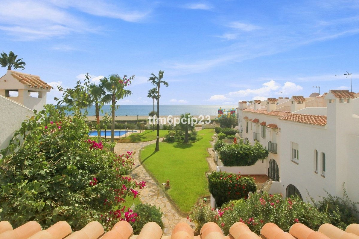 View from a balcony overlooking a garden with a pool, palm trees, and the beach in the distance.
