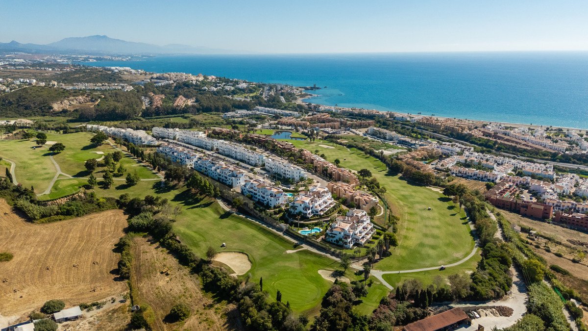 Aerial view of modern apartments and villas on a golf course with the Mediterranean Sea in the background.