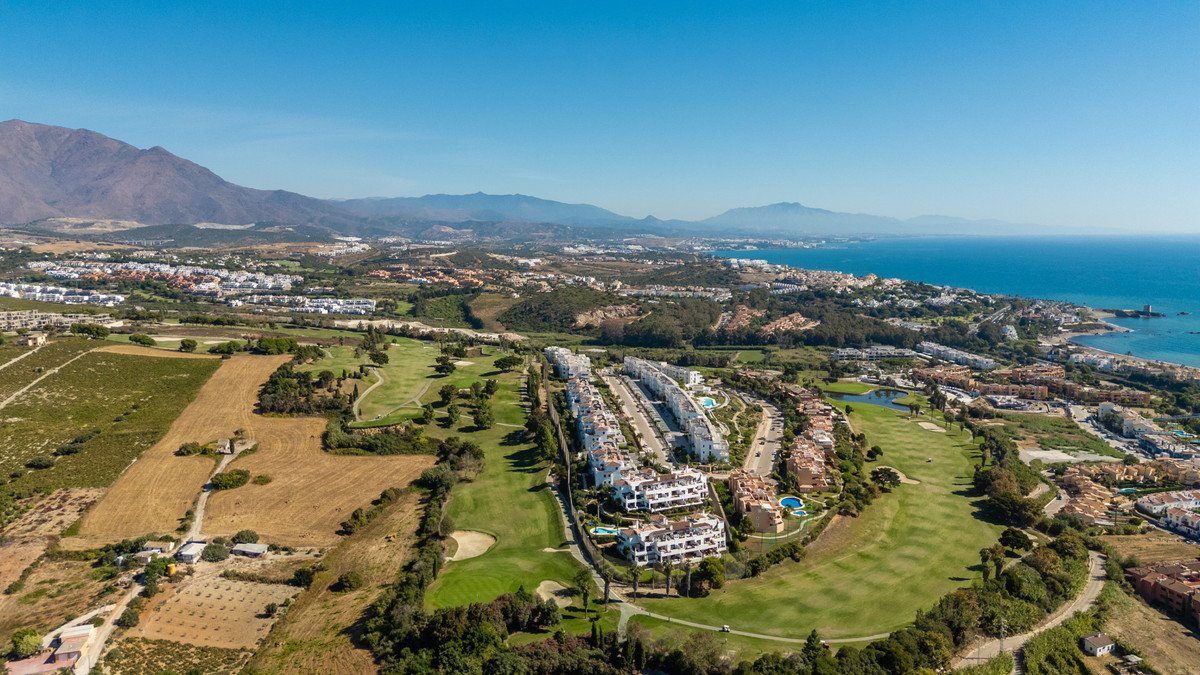 Aerial view of modern apartments situated on a golf course, with a scenic view of the sea and mountains in the distance.