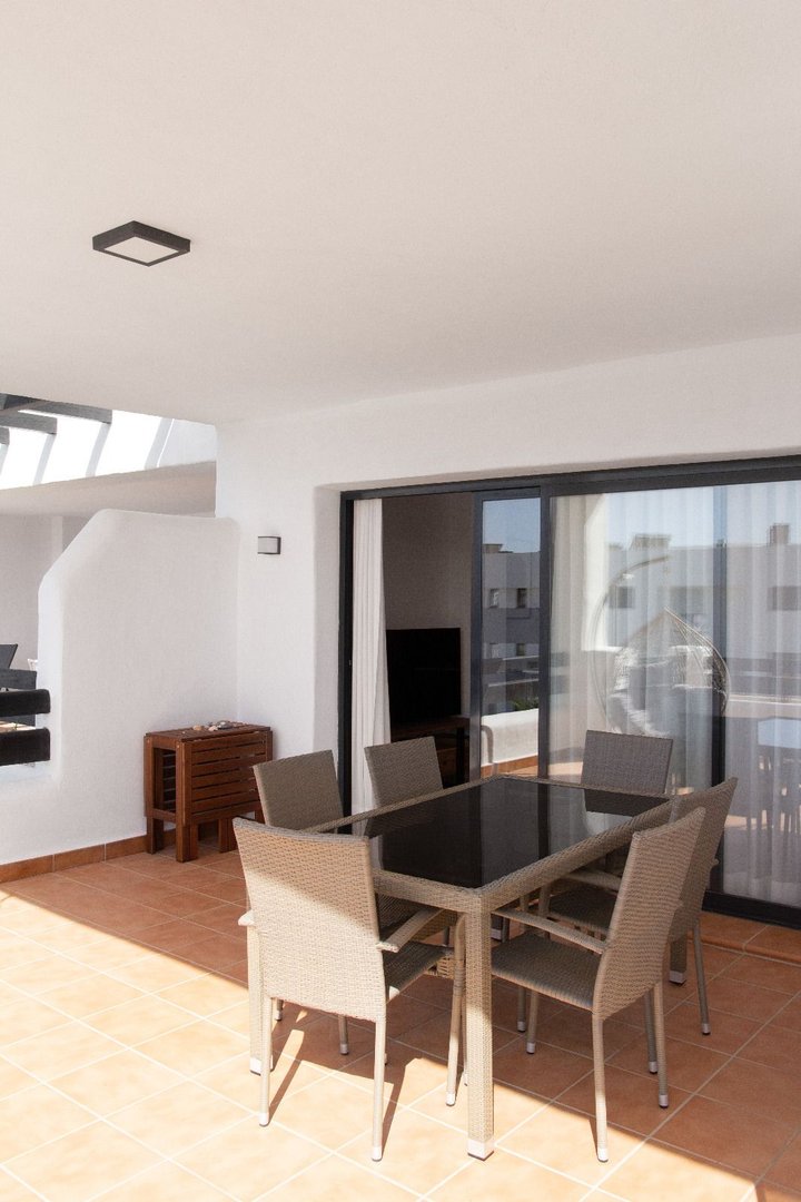 Outdoor dining set with chairs on a tiled terrace, offering a view through sliding glass doors.
