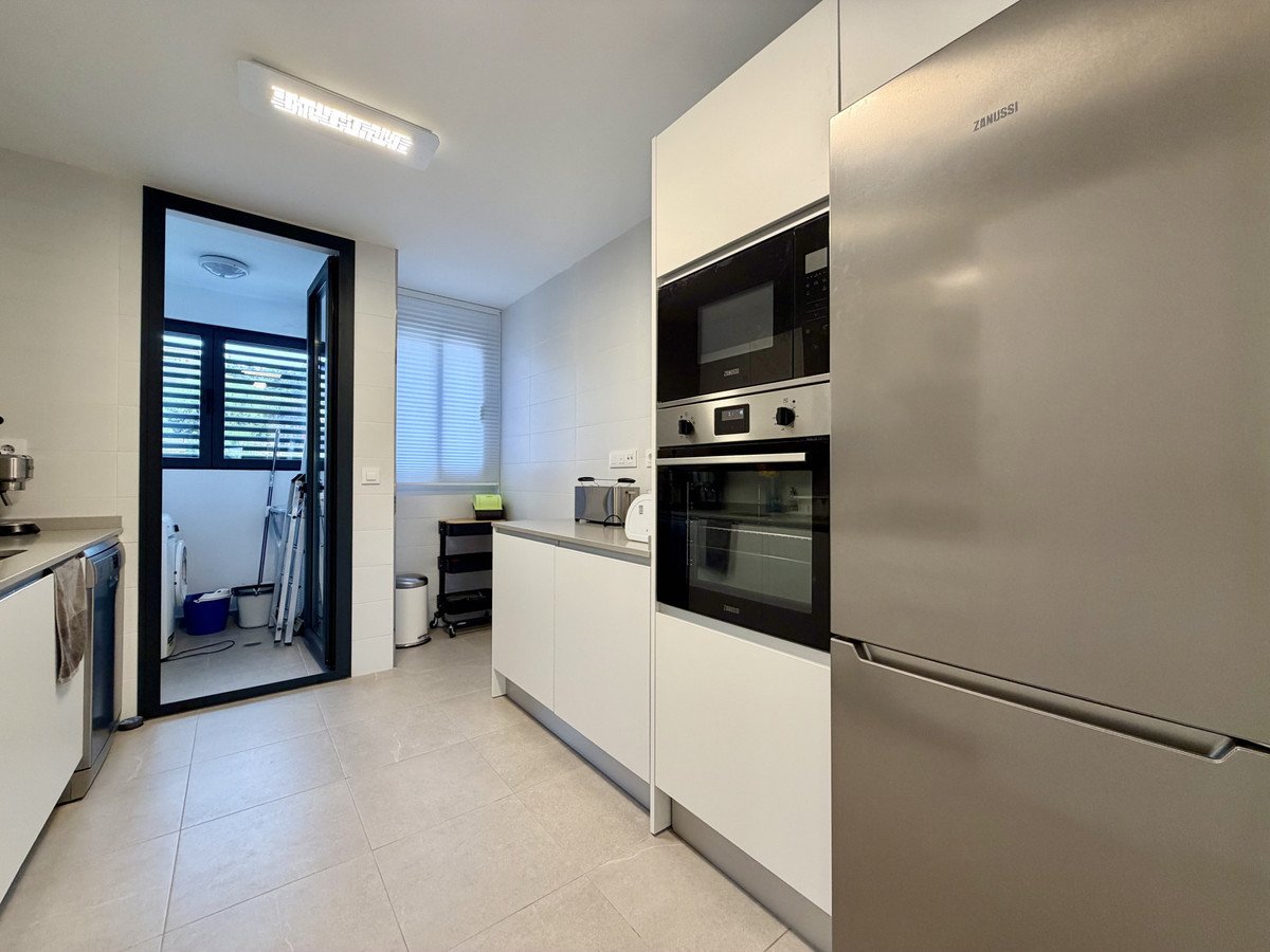 Modern kitchen with stainless steel appliances, built-in oven and microwave, and view to a utility room with laundry facilities.