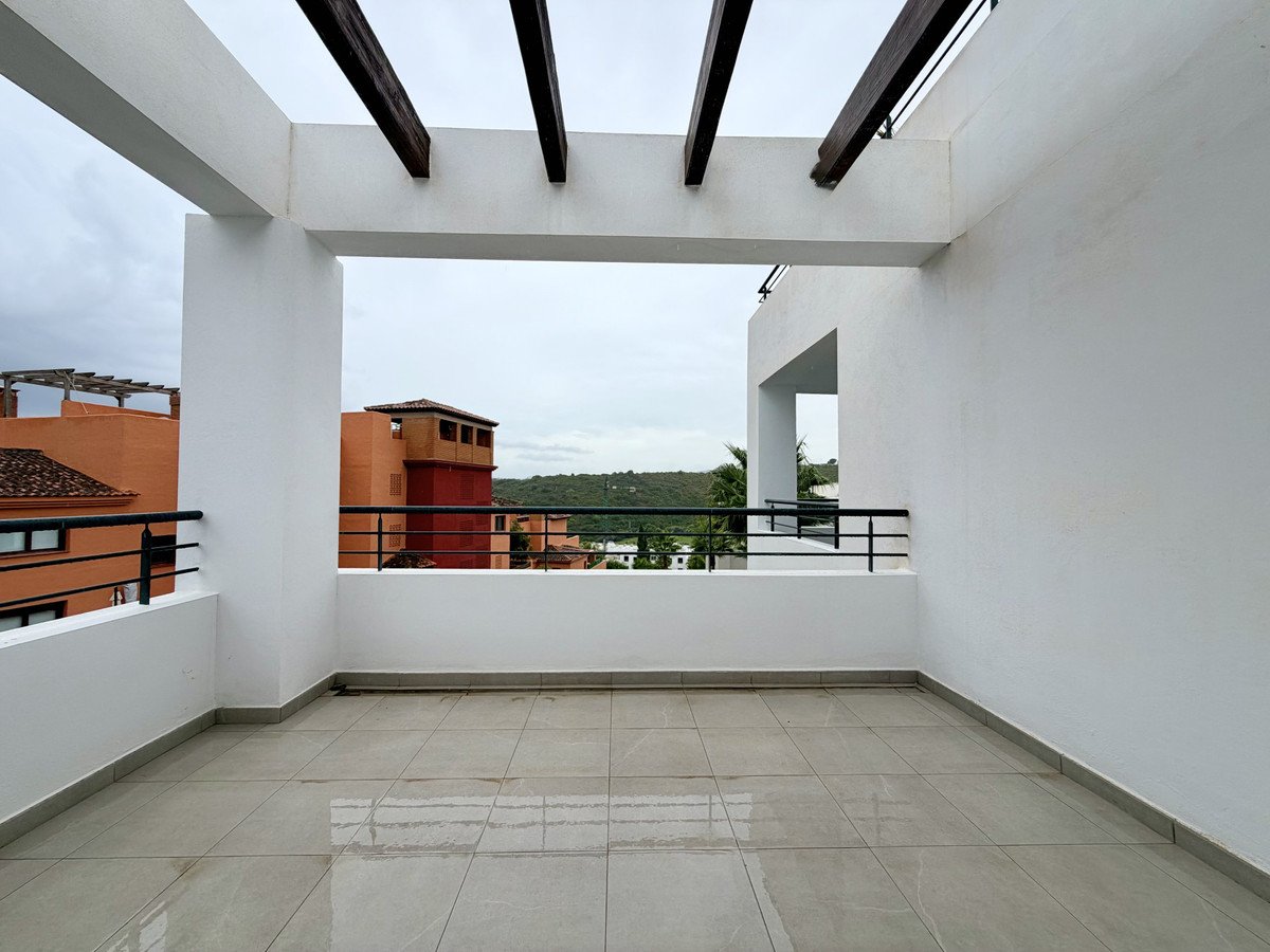 Spacious modern terrace with white walls, black railings, and a view of surrounding buildings and hills.