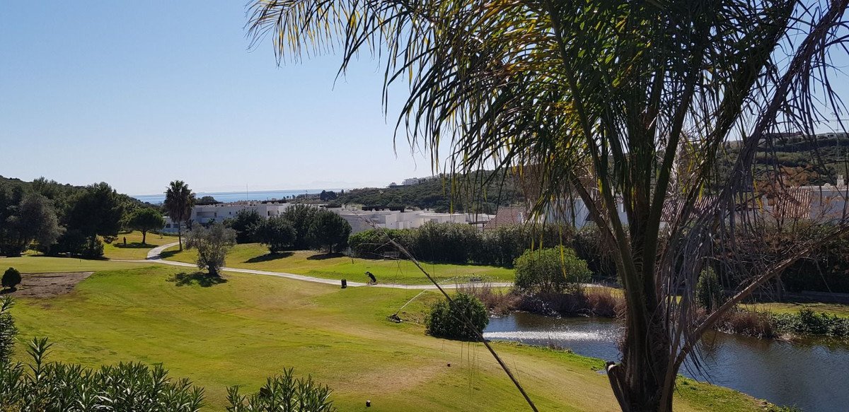 Vila com vista para campo de golfe, palmeiras e lago sob céu azul.