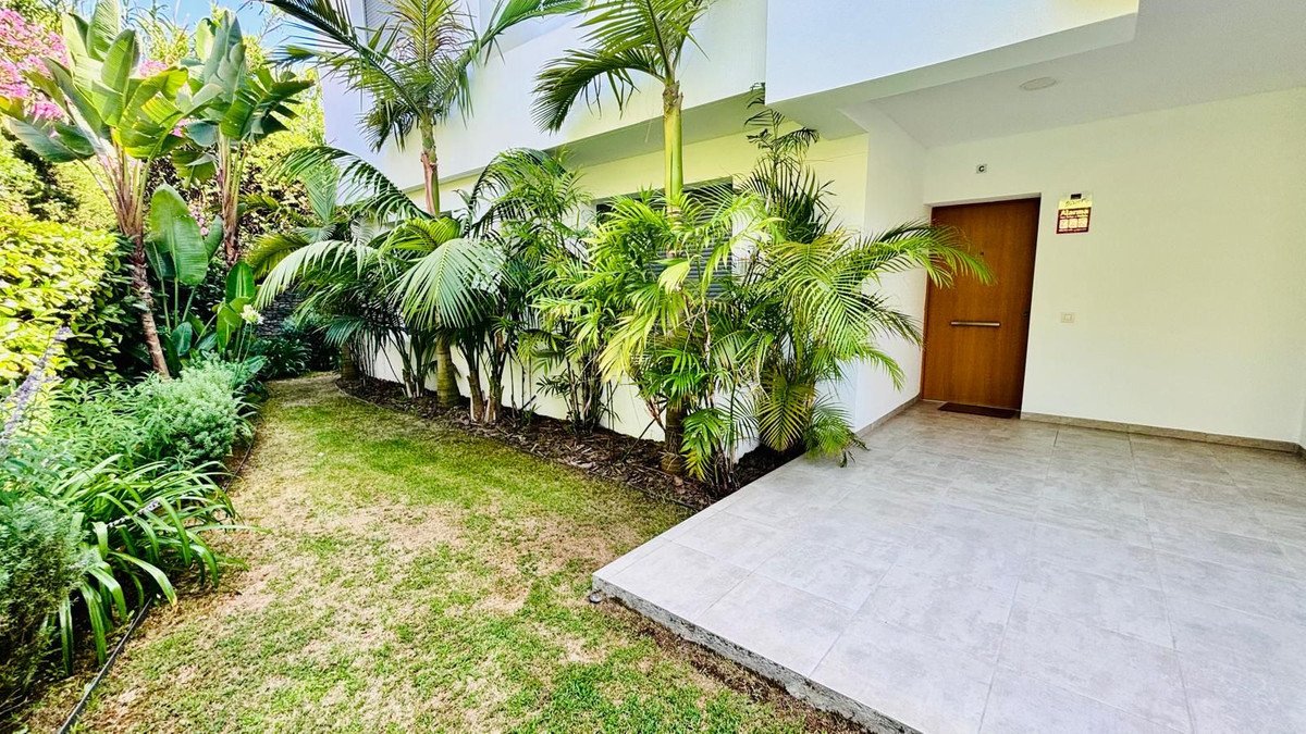 Modern home entrance with tiled patio, lush tropical plants, and a wooden door.