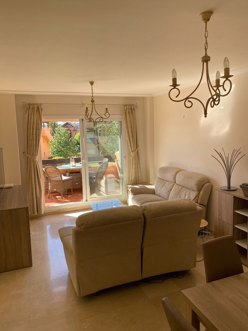 Living room with beige sofas, chandelier, and sliding glass doors leading to a terrace with outdoor seating.