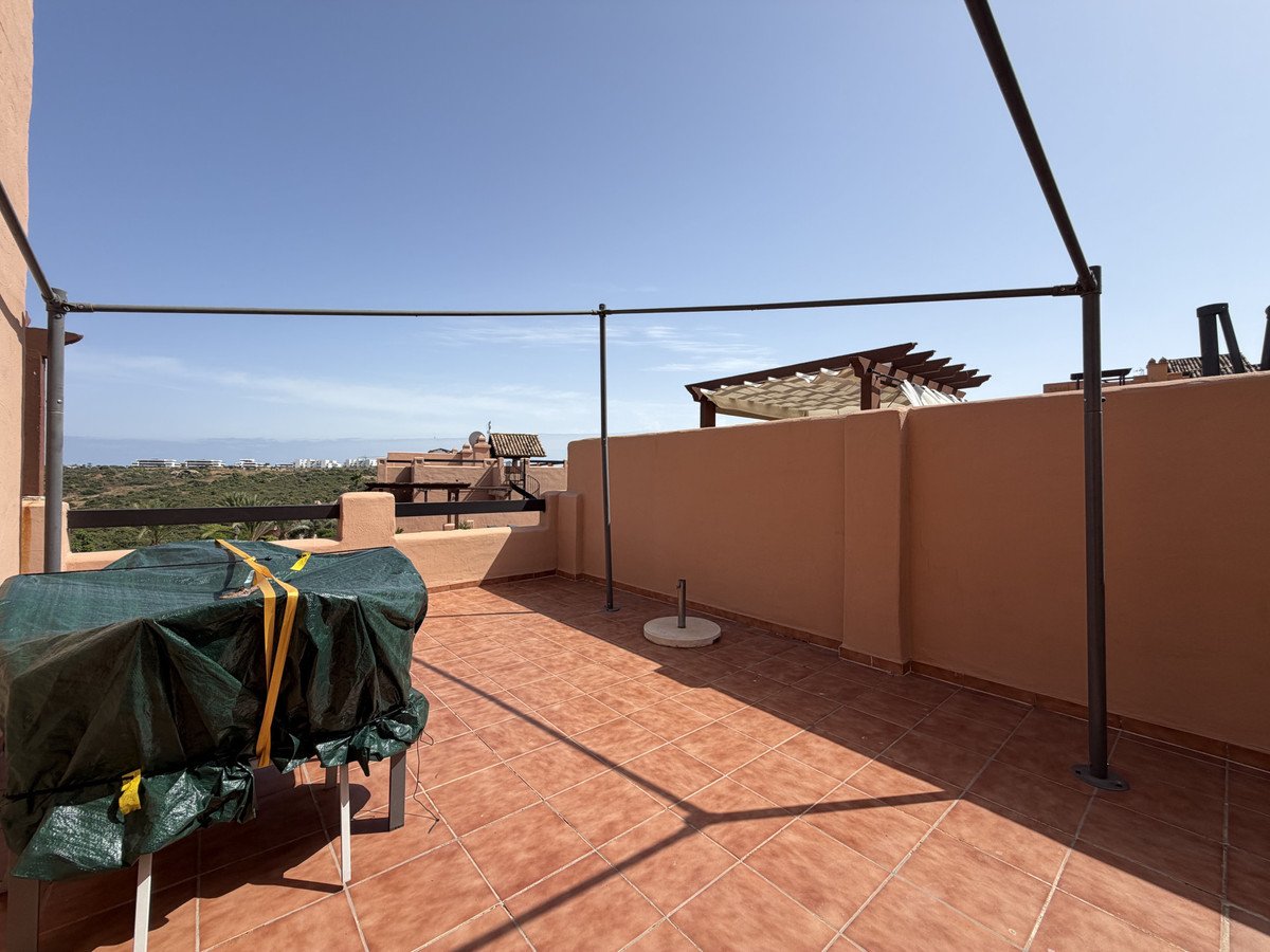 A tiled terrace with a covered table and a metal pergola structure, offering a distant view of the sea and buildings.